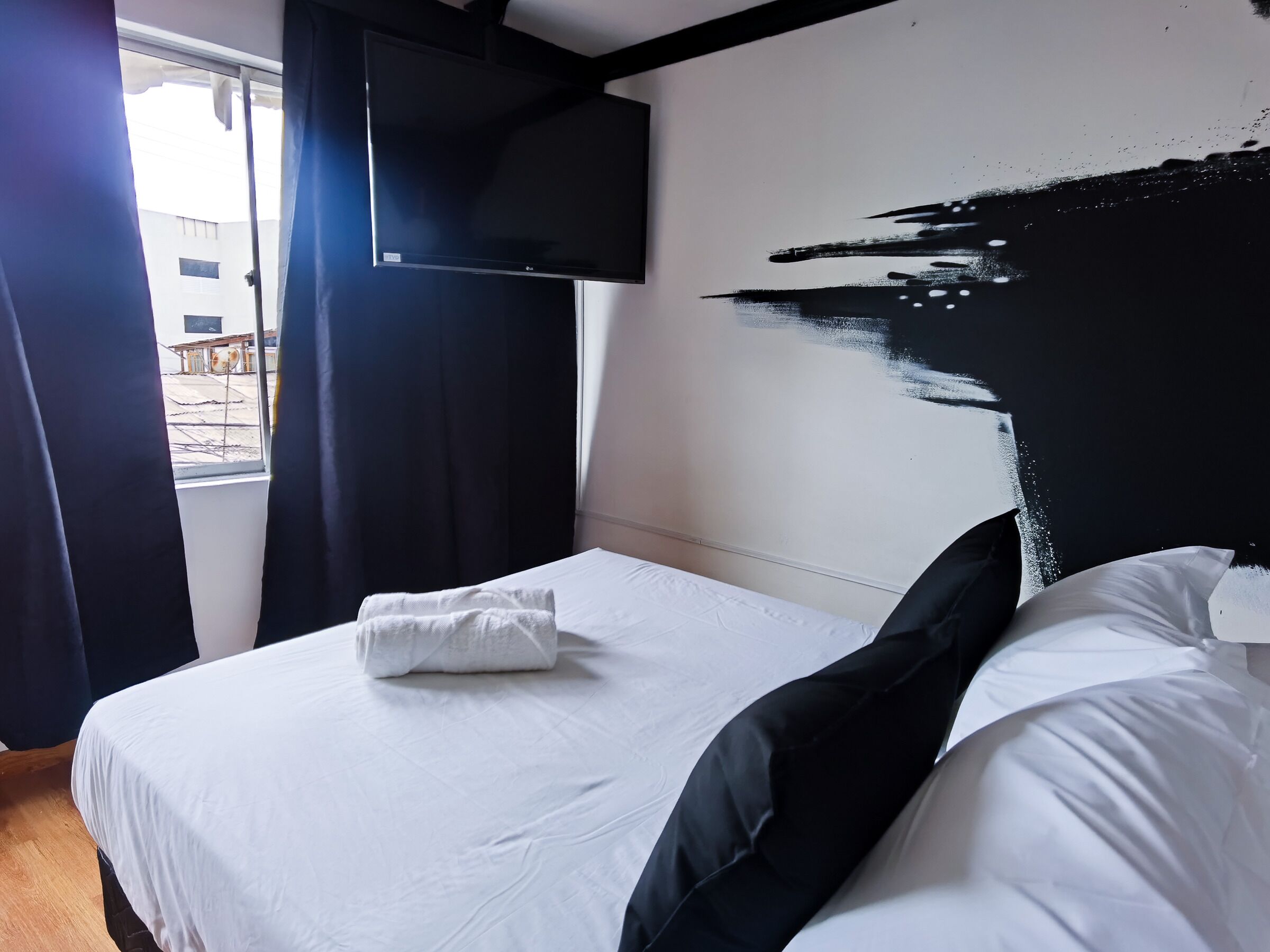 Habitación de hotel con cama, televisor de pantalla plana en la pared y ventana con cortinas.