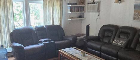 A living room with a wooden ceiling, two black leather sofas, a coffee table, and a large window with curtains.