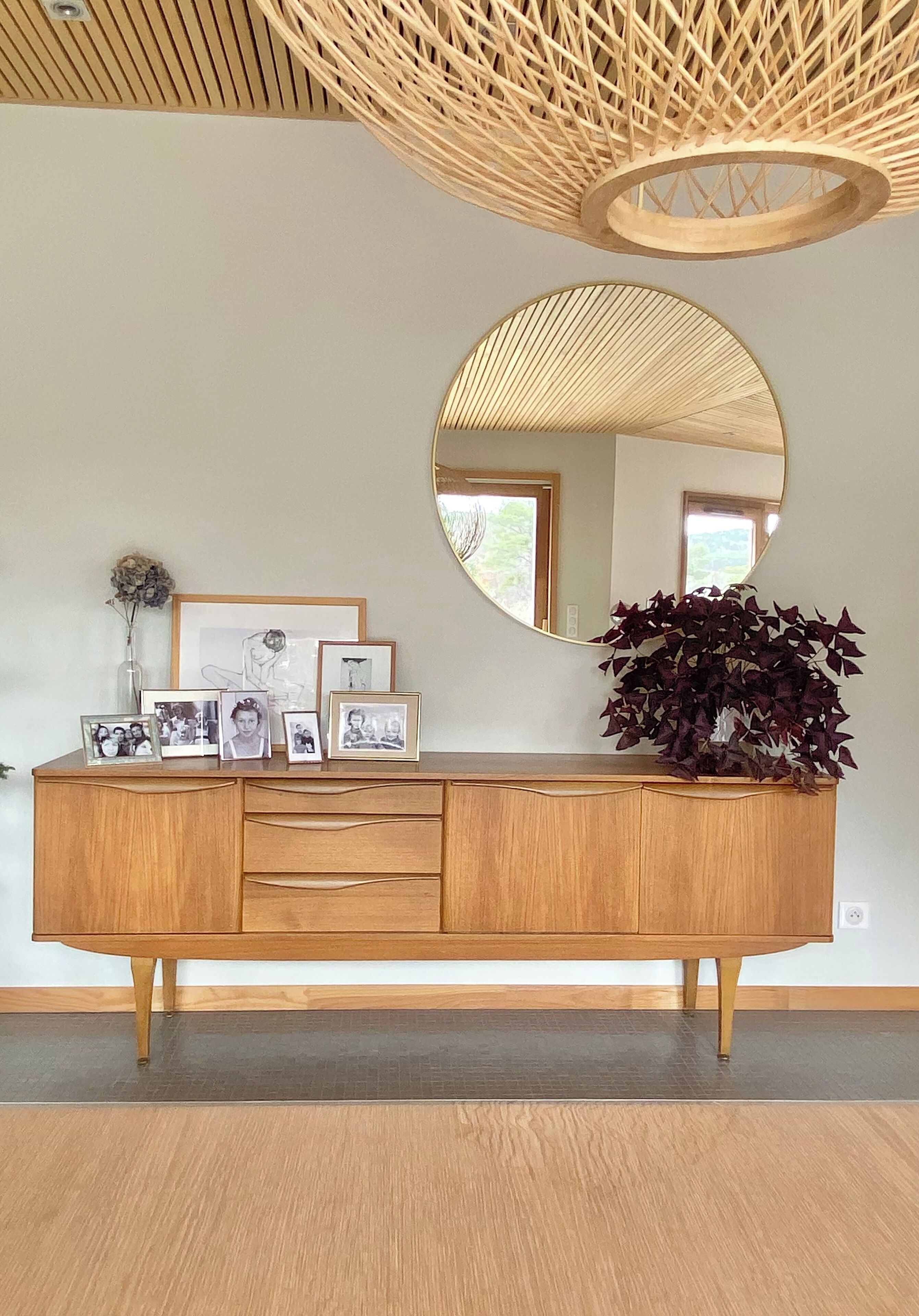 A wooden cabinet with framed photos, a mirror, and a potted plant.