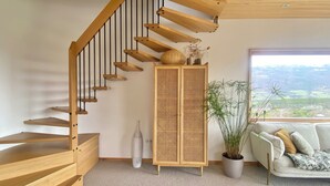 Eine Holztreppe mit einem Rattankorpus und einem Topfpflanzen neben einem Sofa mit Blick auf die Landschaft.