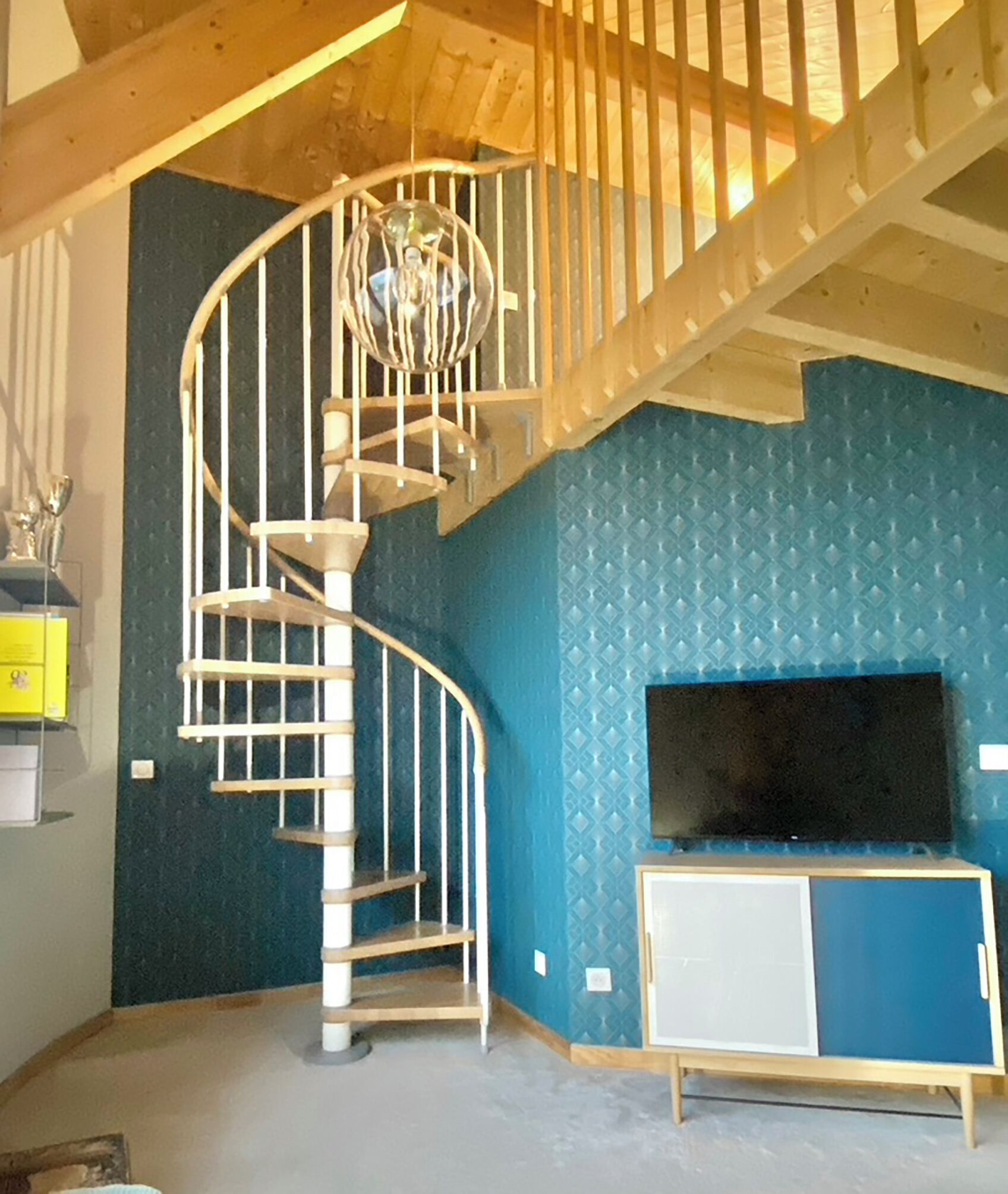 A spiral staircase in a room with blue patterned walls, a TV stand, and a wooden ceiling.