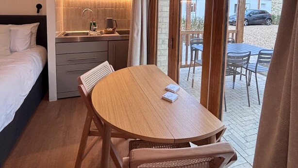 Une chambre d’hôtel compacte comprenant un lit, une kitchenette, une table à manger et une porte-fenêtre coulissante donnant sur un patio extérieur.