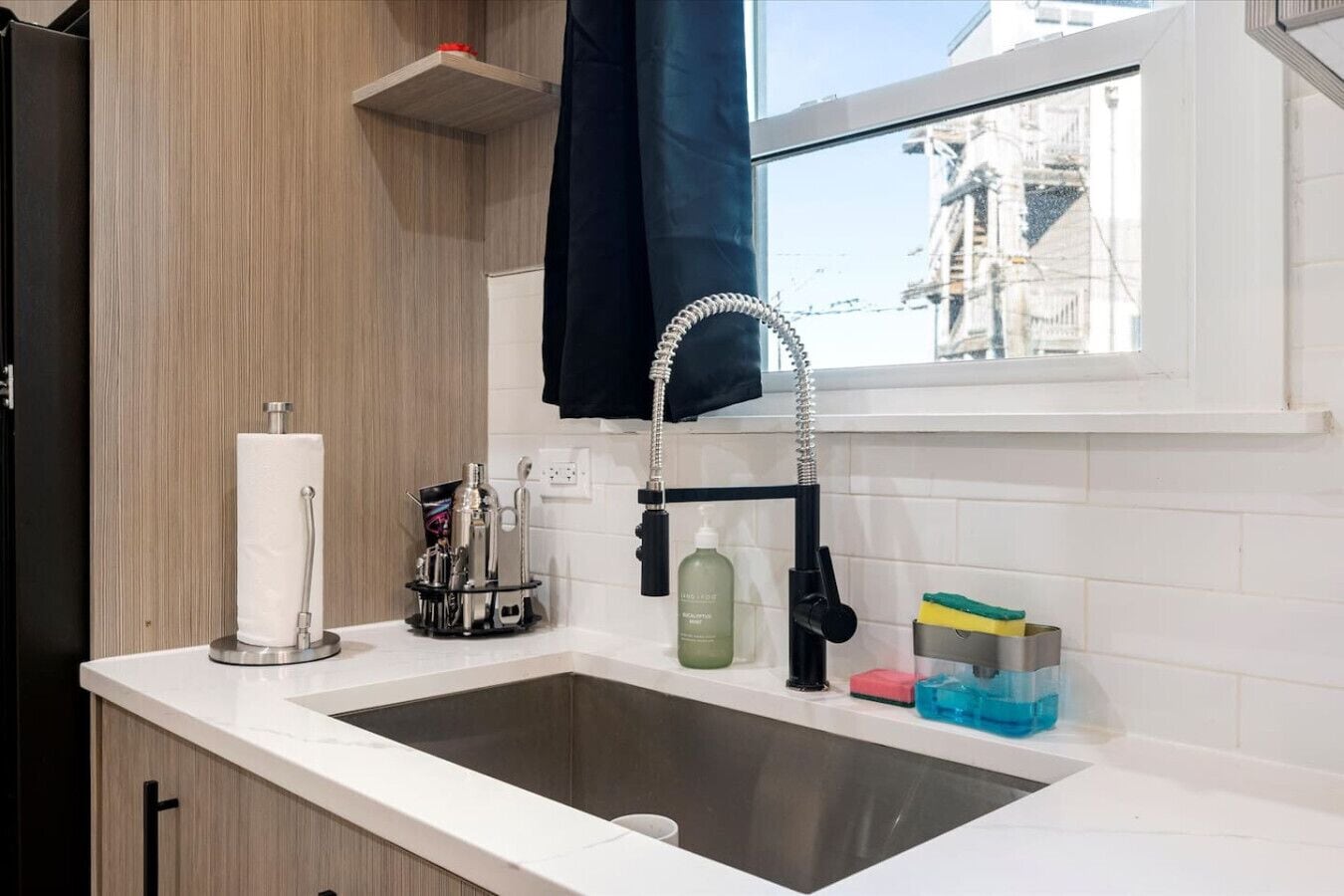 A modern kitchen with a sink, a towel dispenser, and a window with a view of buildings.
