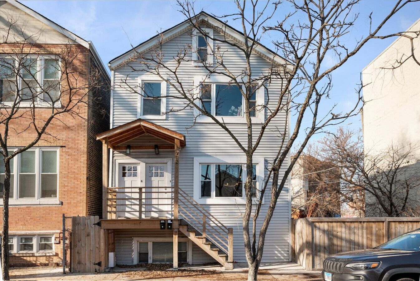 A two-story house with a front porch, a staircase leading to the second floor, and a fenced yard.