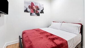 Ein Schlafzimmer mit einem Bett, weißer Bettwäsche, einer roten Decke und einem an der Wand befestigten Kunstwerk.