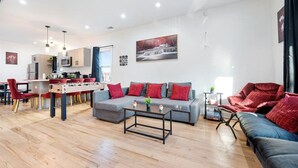 Ein modernes Wohnzimmer mit einer Couch, einem Couchtisch und roten Sesseln. Es gibt eine Küchenzeile mit einem Esstisch und Stühlen.