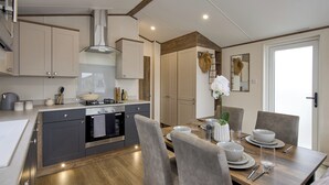 A modern kitchen with grey cabinets, a built-in oven, and a dining area with a wooden table and grey chairs.