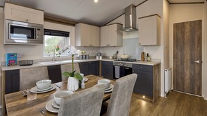 A modern kitchen with a wooden dining table, white plates, and a vase of flowers.