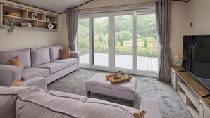 A modern living room with a grey sofa, a coffee table with decorative items, a flat-screen TV, and a large sliding glass door leading to an outdoor deck.
