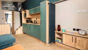 A compact kitchen with green cabinets, a wooden countertop, and a radiator. - Azure Horizons– Retreat Hot Tub Glamping Pod PF GV08 (Northampton)