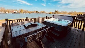 Ein Whirlpool auf einer Holzterrasse mit Blick auf einen See und Gebäude im Hintergrund.