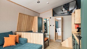 A modern interior with a sofa, wooden panel walls, a staircase, and a small kitchen area. - Azure Horizons - Brook Glamping Pod Pet GV19 (Northampton)