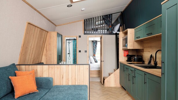A compact living space with a kitchenette, a sofa with cushions, a staircase, and a view to a bathroom. - Azure Horizons - Brook Glamping Pod Pet GV19 (Northampton)