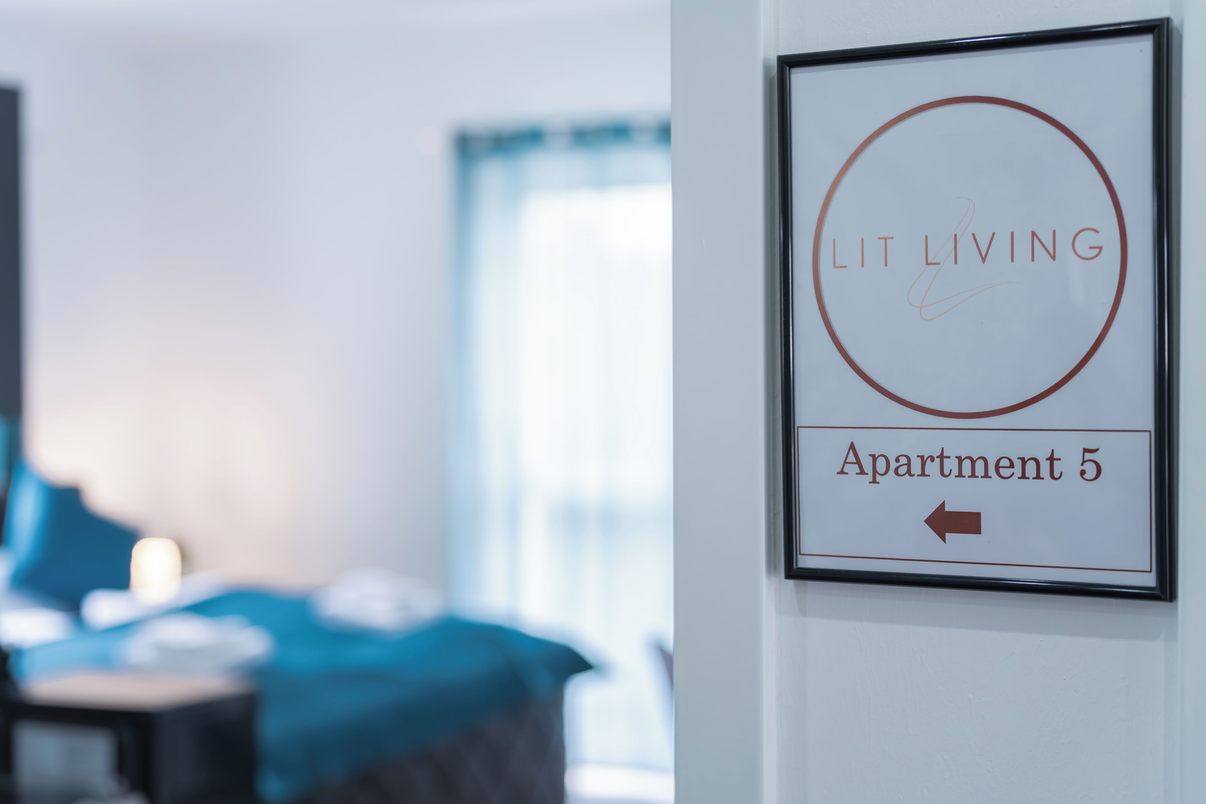 Ein gerahmtes Schild mit der Aufschrift 'Lit Living' und 'Apartment 5', ein Pfeil zeigt nach links.