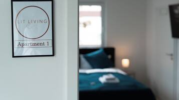 A framed sign on a wall, a bed with a blue cover, and a window with daylight.