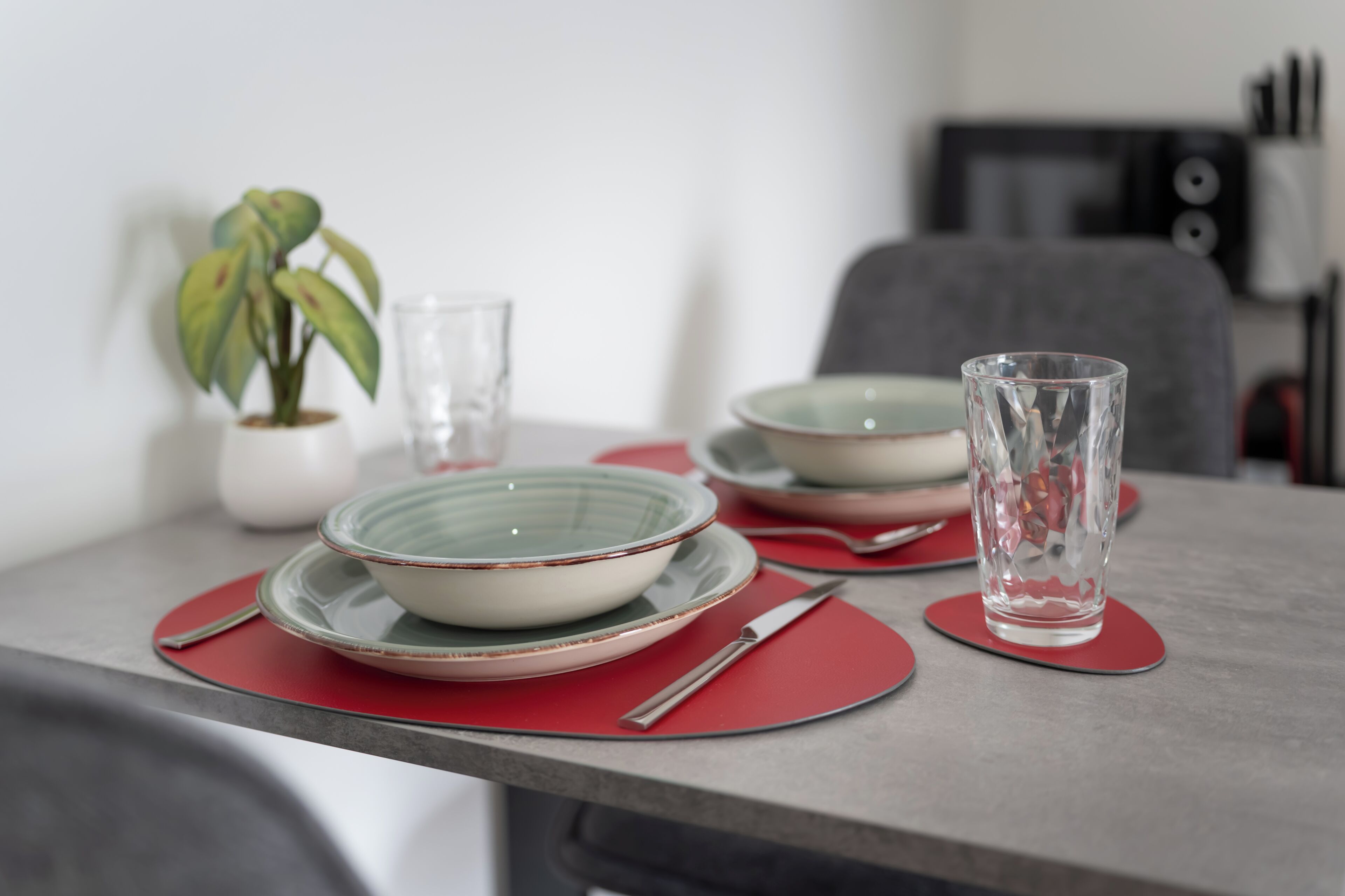 A dining table with red placemats, a glass, and bowls.