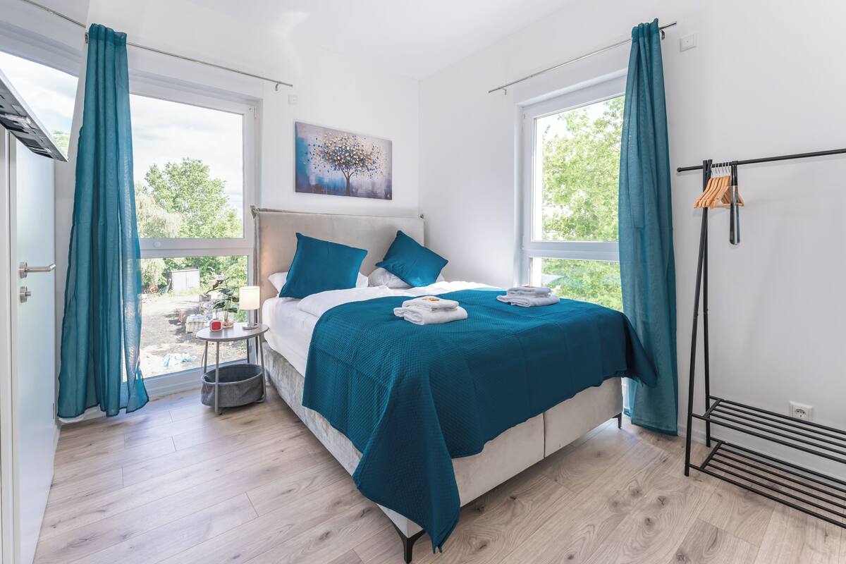 A modern bedroom with a bed, teal curtains, a window, and a painting.