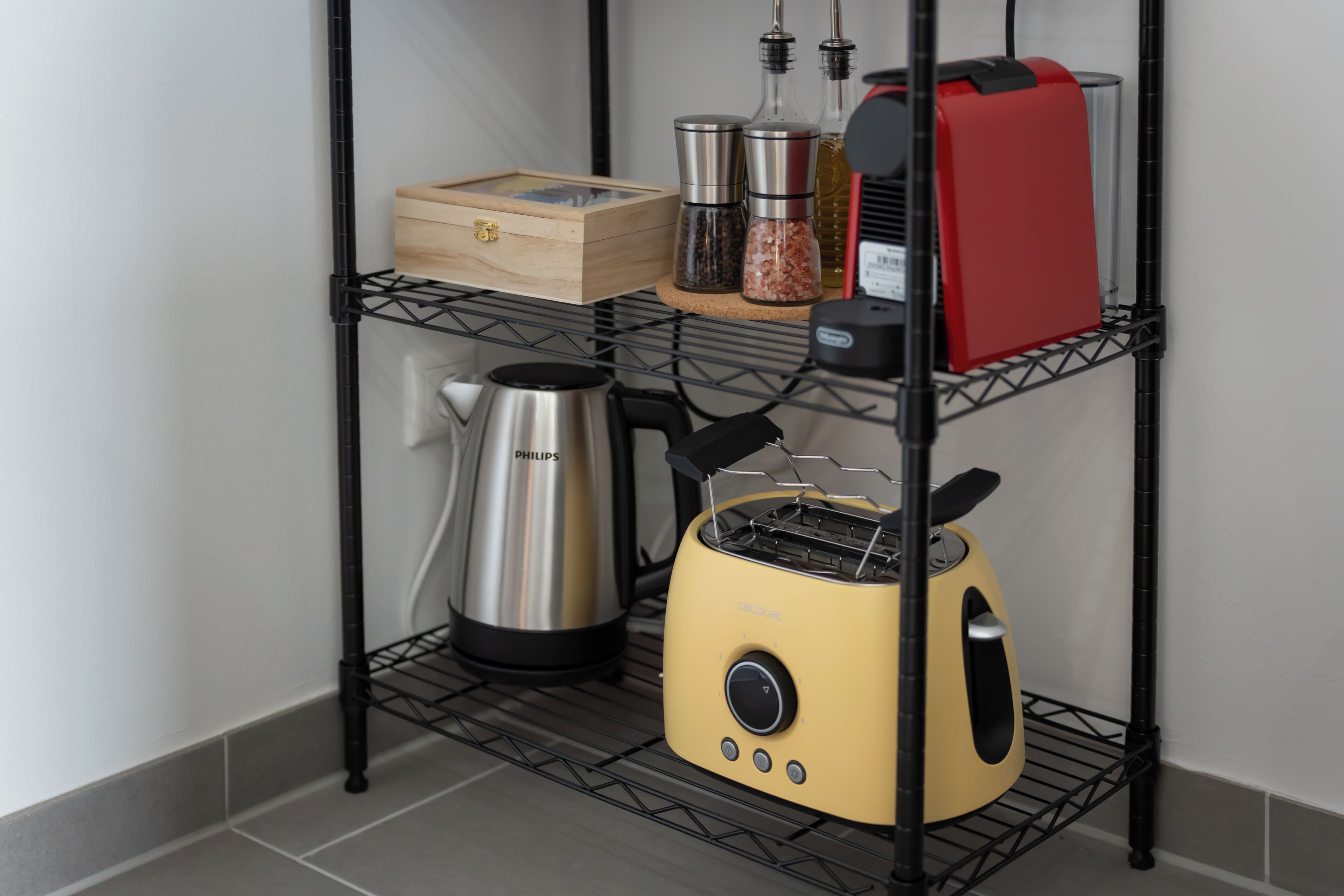 A kitchen area with a black metal shelf holding a toaster, a kettle, and a spice rack.