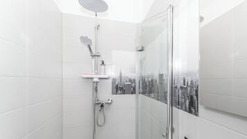 A modern bathroom with a glass shower enclosure, white tiled walls, and a cityscape view.