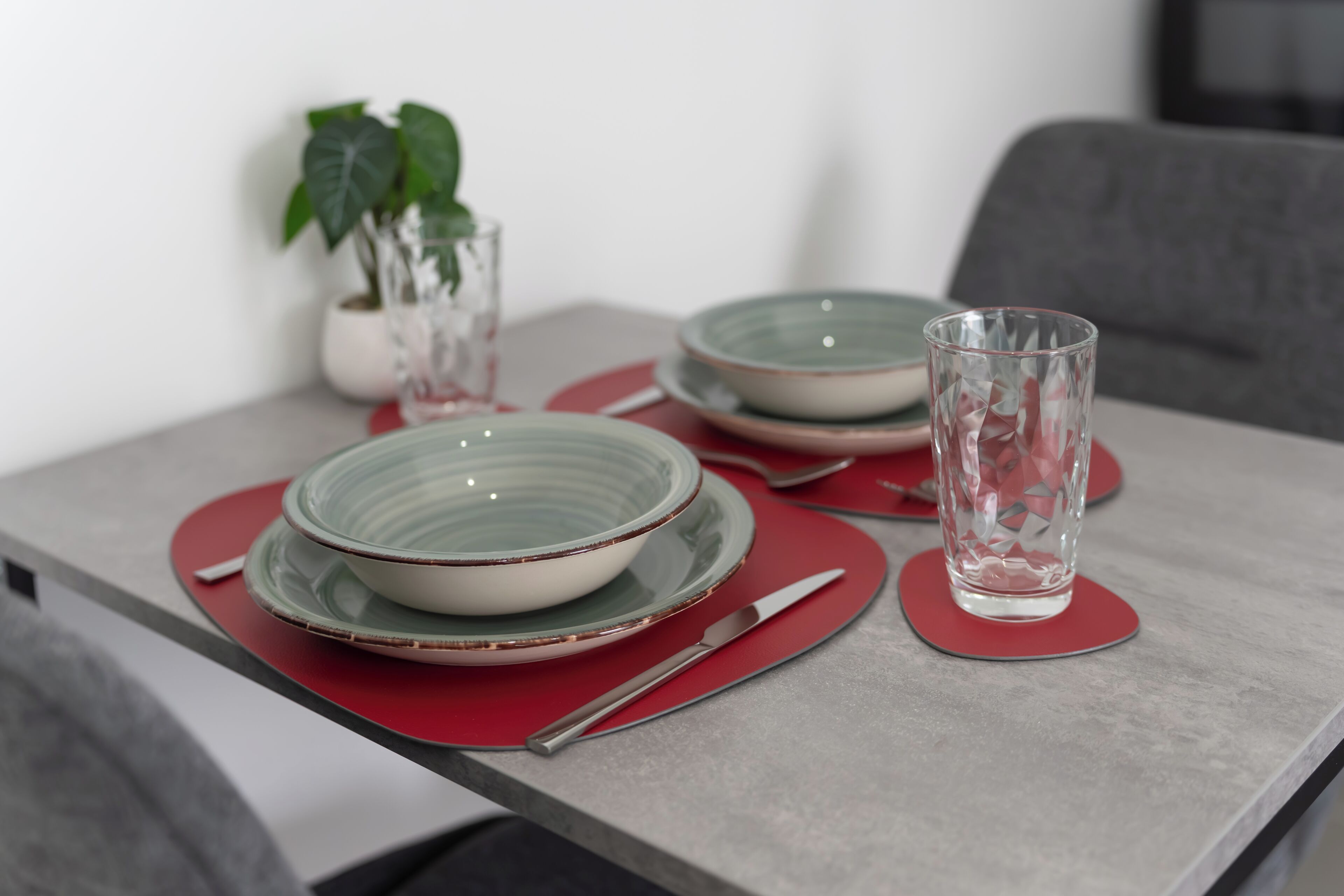 A dining table with red placemats, a glass, and bowls.