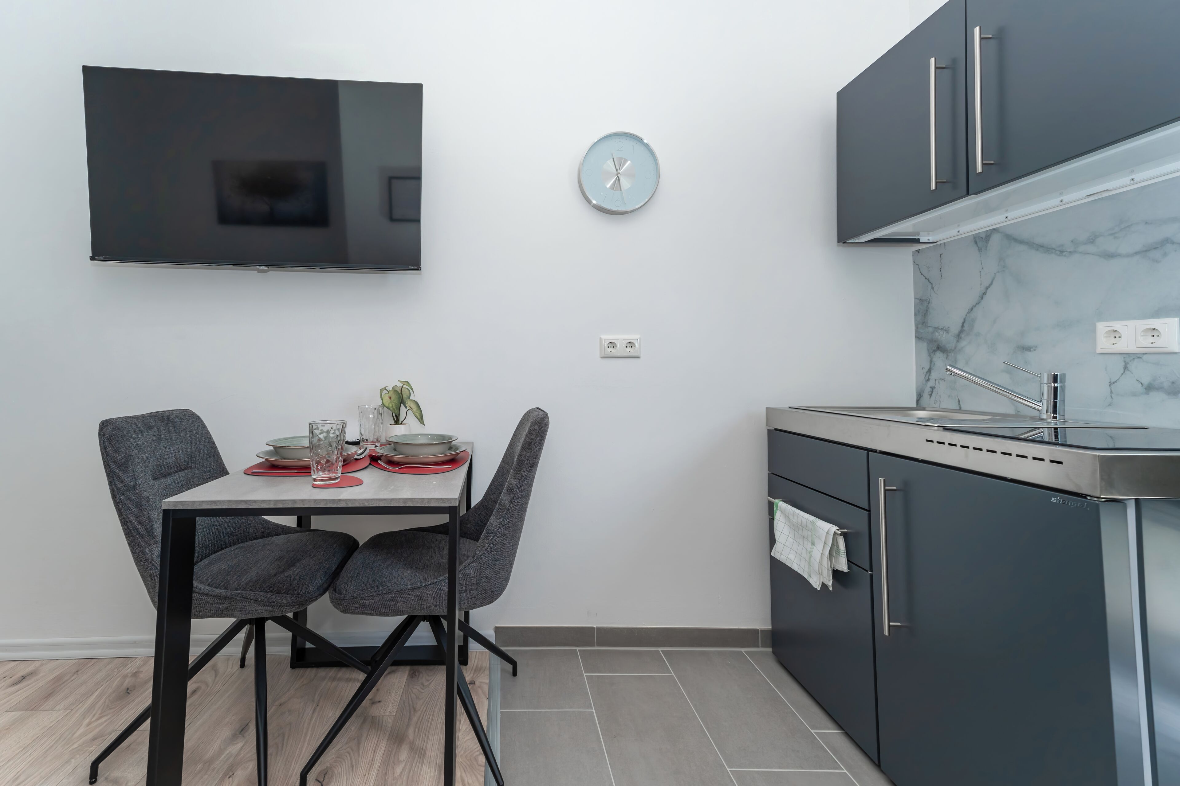 Una cocina moderna con armarios grises, un lavamanos de acero inoxidable y un televisor de pantalla plana montado en la pared.