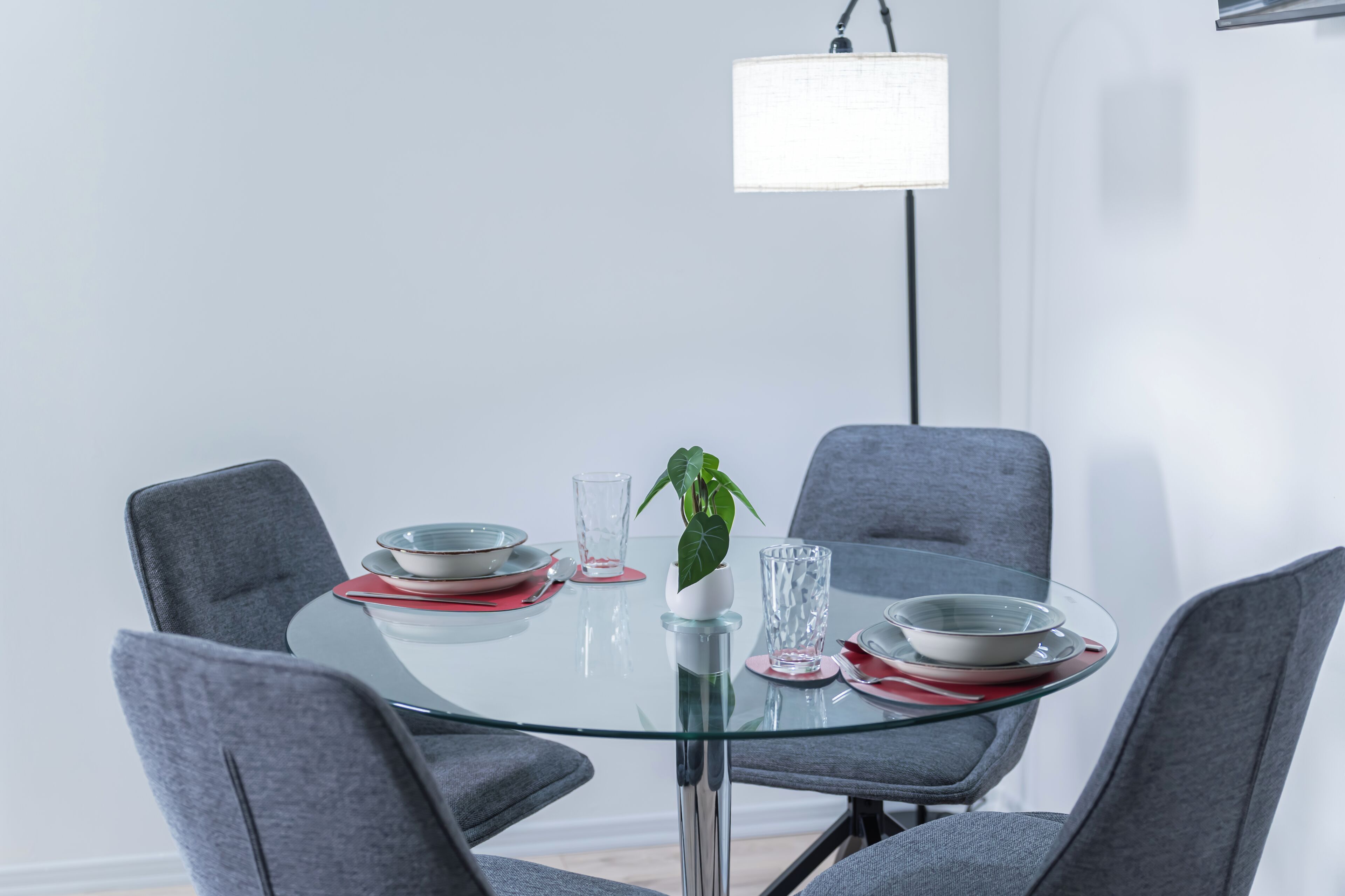 A modern dining table with glass top and grey chairs, a potted plant, and a hanging light fixture.