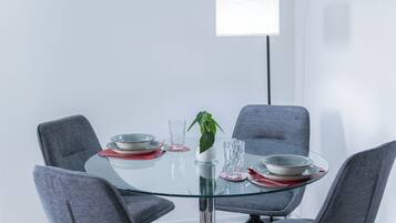 A modern dining table with glass top and grey chairs, a potted plant, and a hanging light fixture.