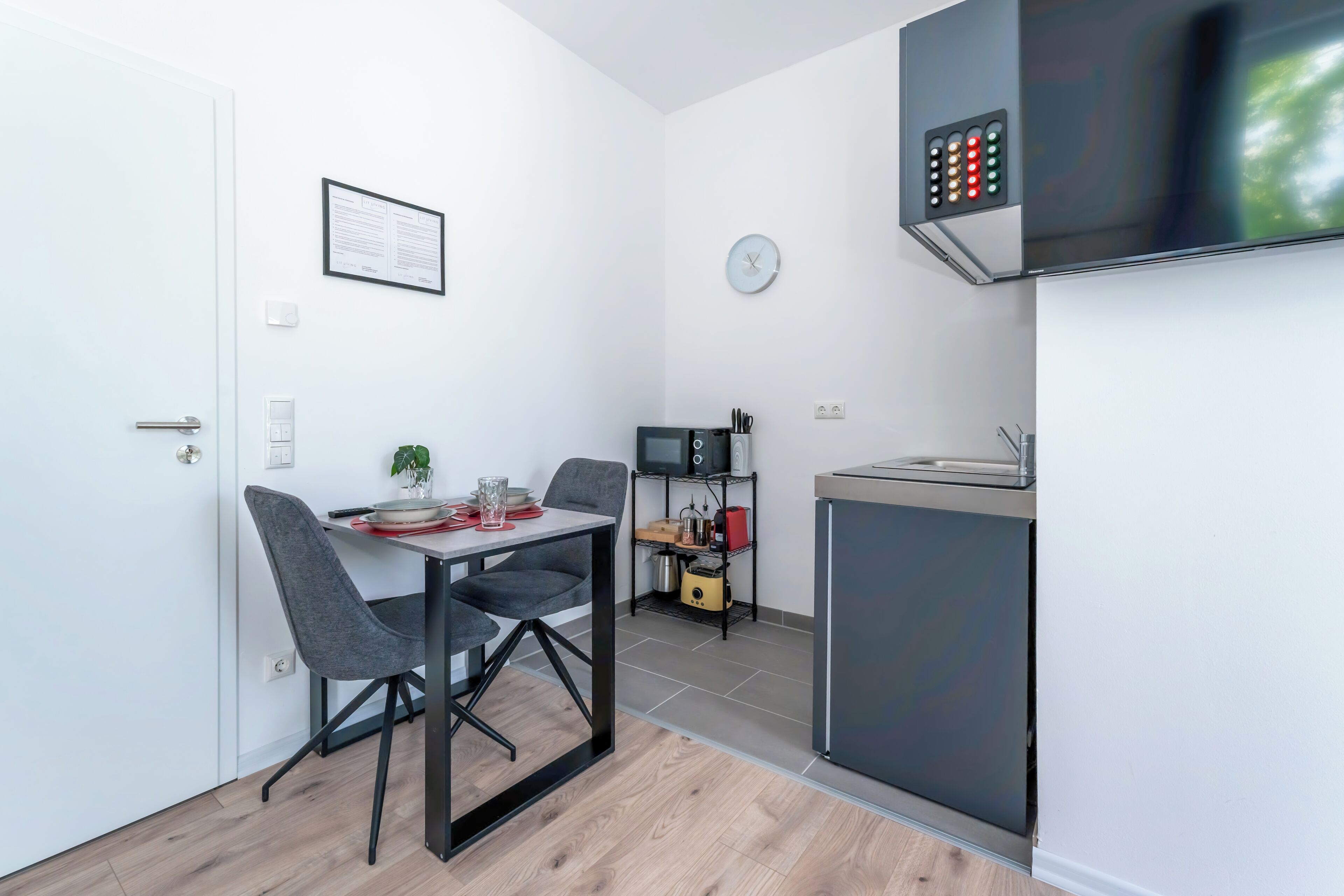 A compact kitchen with a microwave, a small fridge, and a clock on the wall.