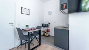 A compact kitchen with a microwave, a small fridge, and a clock on the wall.