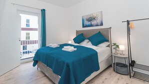 A modern bedroom with a bed, a bedside table with a lamp, a small plant, and a view of the outside balcony. - Lit Living-Luxury-Box Spring - Parking (Altenstadt)