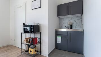 A compact kitchen with a dark grey cabinet, a microwave, and a small shelf with kitchen items.