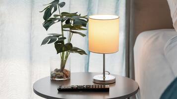 A bedside table with a remote control, a lamp, and a potted plant with a glass container of rocks.