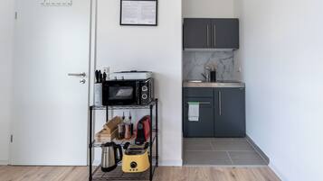 A compact kitchen with a microwave, toaster, and kettle on a shelf, a small countertop, and dark cabinets.