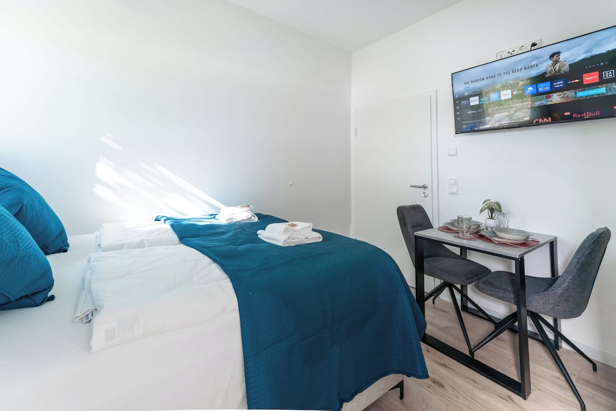 A hotel room with a bed, a desk, and a TV mounted on the wall.