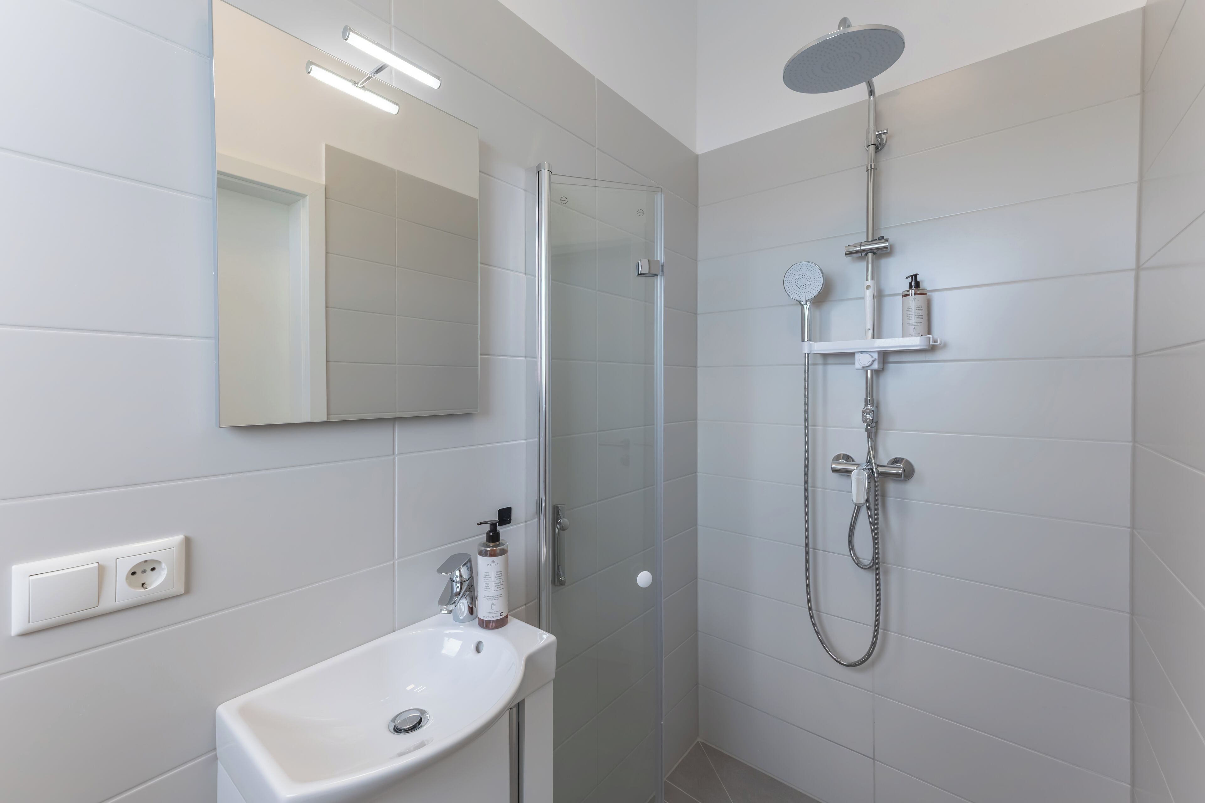 A modern bathroom with a glass-enclosed shower, a white sink, and a mirror above it.