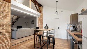 A modern kitchen with a wooden countertop, two bar stools, and a dining table. - Le Duplex du Castel haut - Escapade Tarnaise (CASTELNAU DE MONTMIRAL)