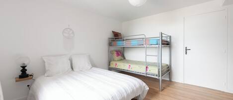 Ein Schlafzimmer mit Etagenbett, einem Einzelbett, einem Nachttisch mit Lampe und einem an der Wand hängenden Traumfänger.