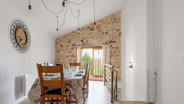 A dining area with a rustic stone wall, a wooden table set for four, and a view of greenery outside. - Le Duplex du Castel haut - Escapade Tarnaise (CASTELNAU DE MONTMIRAL)