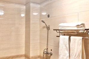 A shower with a handheld showerhead, a towel rack with folded towels, and a wall-mounted towel rack. - Yina Inn (Lijiang Ancient City Dashuiche) (Lijiang)
