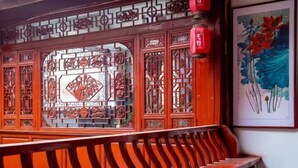 A traditional Chinese-style room with intricate wooden lattice windows, a wooden bench, and a framed painting on the wall.