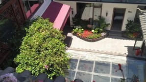 A rooftop garden with a glass balustrade, potted plants, and a small seating area.
