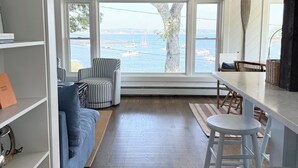 A spacious room with a large window overlooking a body of water, a ceiling fan, and a dining area with a bar. - Five Islands Waterfront Retreat (Georgetown)
