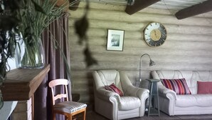Un saló tranquil amb sostre de fusta, un sofà de pell blanca, una cadira de fusta, una taula petita i una planta gran.