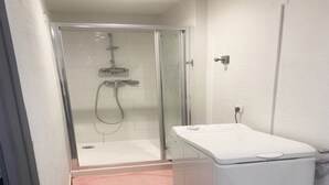 A small, enclosed shower area with a glass door, a white washing machine, and a pink towel on the floor.