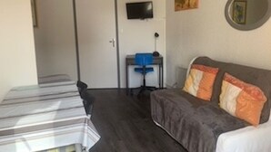 A room with a bed, a desk, a chair, a television, and a door.