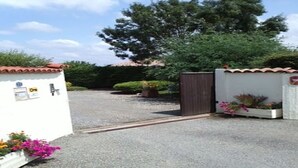 A gated entrance with a gravel driveway leading to a building with a white exterior and red-tiled roof.