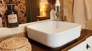 Ein Badezimmer mit einem weißen Waschbecken, einer Dekoflasche, einem gewebten Korb und einer Vase mit Trockenpflanzen.