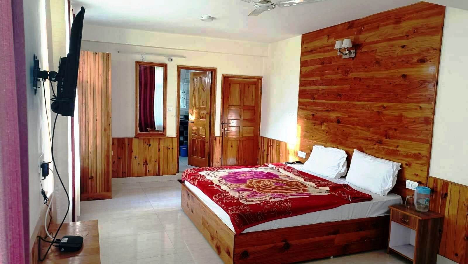 A bedroom with a wooden headboard, a bed with a red and white bedspread, a bedside table with a lamp, and a wooden wardrobe.