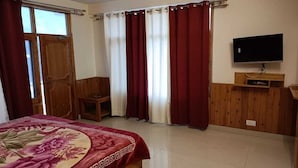 Un dormitorio con cama, televisor, armario de madera y ventana con cortinas.