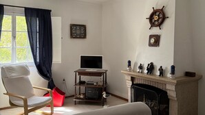 Una sala de estar con chimenea, un televisor sobre un mueble bajo, una silla y una cama.